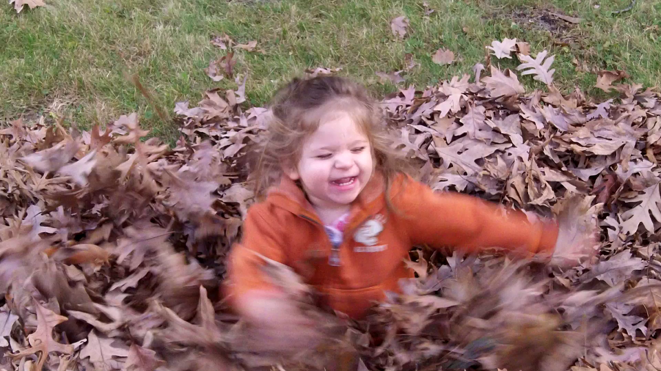 Young girl playing in pile of leaves