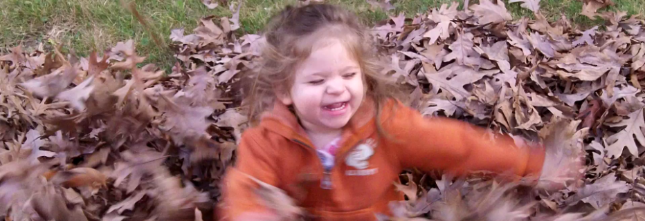 Young girl playing in pile of leaves